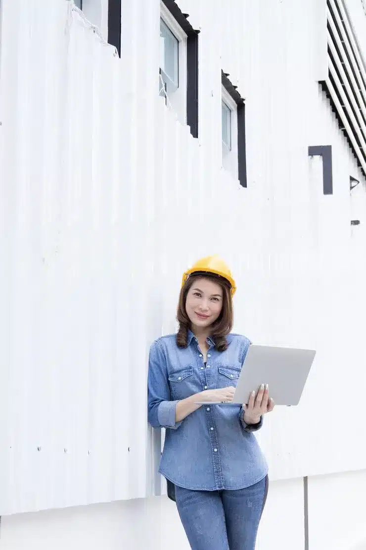 Female jeans wearing yellow safety hat front metal sheet wall construction site